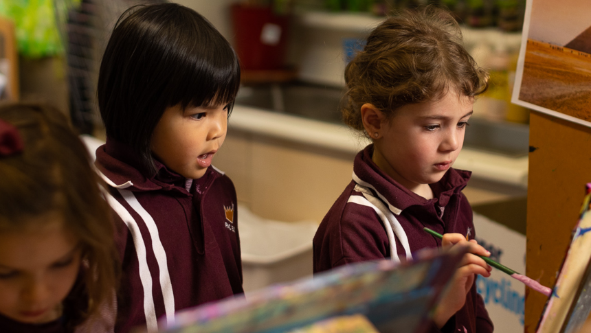 Young pupil watching another pupil paint on an easel