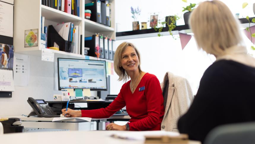 Two female teachers talking at desk in teacher's office.