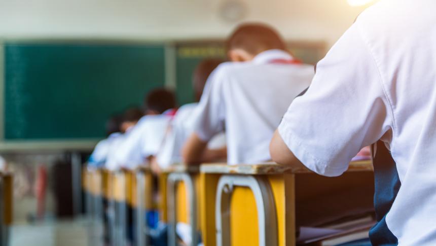 School students taking exam in row of desks in classroom.