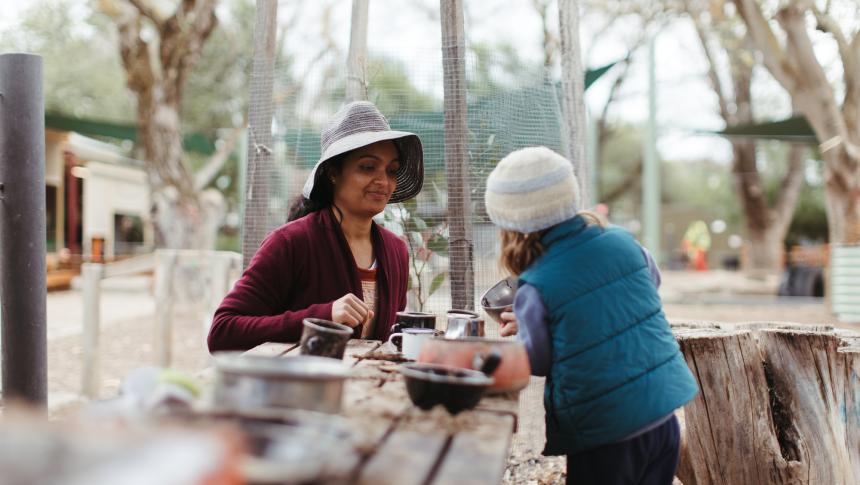 A teacher and a child playing with some bowls and cups at an outdoor playground at an early childhood education and care service. Credit: AERO